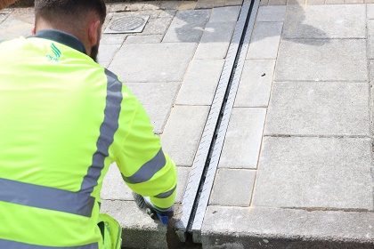 Picture of a man in a high vis jacket bending down over a new gully installation.