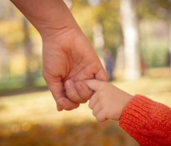 Photo of a parent’s hand holding a young child by their index finger.