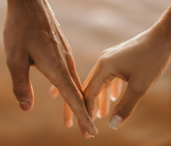 Photo of two hands with fingers lightly touching each other and interlocking.